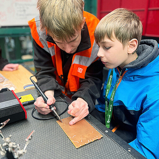 Hannes, Elektroniker für Geräte und Systeme im 2. Ausbildungsjahr, zeigt, wie's geht: Beim Löten eines elektronischen Würfels werden Widerstände, Kondensatoren und LEDs direkt auf der Platine verbaut.