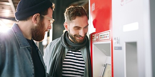 Zwei Personen schauen auf den Bildschirm eines Ticketautomaten