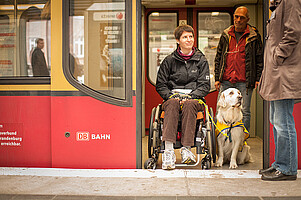 A woman in a wheelchair is accompanied by a dog in the train.