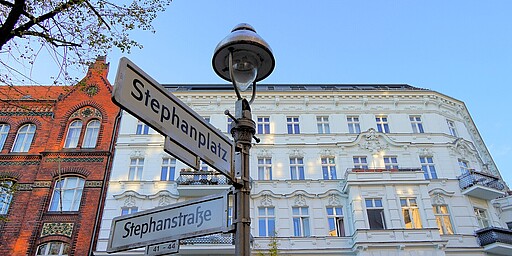 Straßenschilder am Stephanplatz Zwei Straßenschilder zeigen „Stephanplatz“ und „Stephanstraße“, mit einer historischen Laterne und einem weißen Altbau im Hintergrund.