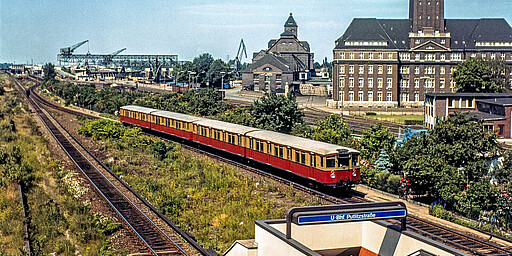 Westhafen Ein Halbzug der Zuggruppe A der Ringbahn verlässt 1978 den Bahnhof Putlitzstraße Richtung Westen. Im Vordergrund der neu eröffnete Zugang von der Ringbahn zur U-Bahnlinie 9. Im Hintergrund ist der Westhafen mit dem mächtigen Verwaltungsgebäude mit seinem 52 Meter hohen Turm zu sehen. Ganz links ist der nächste Bahnhof Beusselstraße mit der Kehranlage für die Züge der Siemensbahn und der Zuggruppe N nach Spandau-West zu erkennen.
