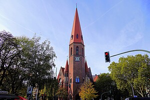 Die imposante Heilige-Geist-Kirche mit ihrem hohen roten Turm, umgeben von herbstlich gefärbten Bäumen, unter einem klaren blauen Himmel.