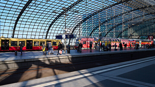 Fahrgäste am Berliner Hauptbahnhof Wartende Fahrgäste auf dem Bahnsteig im Berliner Hauptbahnhof mit einer einfahrenden S-Bahn und einem stehenden Regionalzug im Hintergrund.