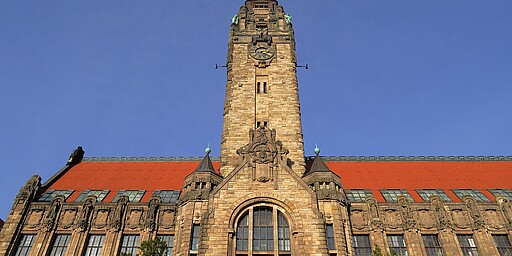 Turm des Rathauses Charlottenburg  Der hohe Turm des Rathauses Charlottenburg, gekrönt von einem großen Zifferblatt und verziert mit Figuren. Das Gebäude zeigt eine rote Ziegeldachkonstruktion und gotische Details an der Fassade, die ihm einen historischen Charme verleihen.