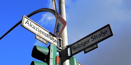 Straßenschilder Akazienstraße und Belziger Straße Ein Straßenschild an einer Ampel zeigt die Kreuzung von Akazienstraße und Belziger Straße in Berlin. Der Himmel ist strahlend blau.
