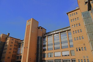 Ein historisches Industriegebäude der Osram-Höfe in Berlin, geprägt durch rote Backsteinfassaden und große Fenster. Im Vordergrund ragen moderne Gebäudeteile in den blauen Himmel und kontrastieren mit der historischen Architektur.