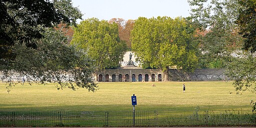 Schillerdenkmal in herbstlicher Pracht Eine Statue von Friedrich Schiller im Schillerpark, umgeben von herbstlich gefärbten Bäumen unter einem leicht bewölkten Himmel.