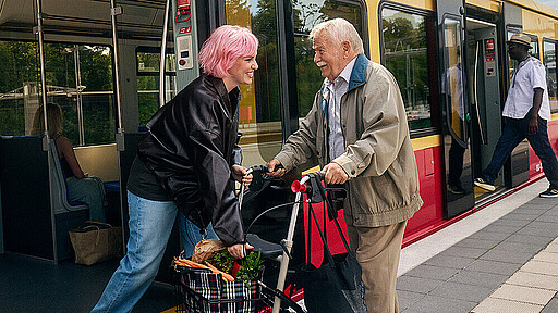 Mehr Verbindung als von A nach B. Eine junge Frau hilft einem älteren Herren mit Rollator in die S-Bahn.