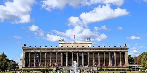 Altes Museum mit Blick auf den Brunnen Vor dem beeindruckenden Altes Museum auf der Berliner Museumsinsel sprudelt ein großer Brunnen. Besucher flanieren auf dem weiten Platz, während der imposante Säulengang des Museums in den Himmel ragt.