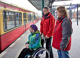 Zwei Begleitpersonen und eine Rollstuhlfahrerin warten auf den Einstieg in den Zug