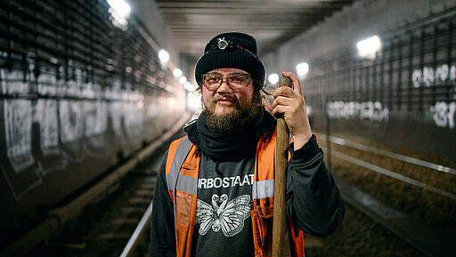 Gleisbauer Pascal Greger stützt sich für das Foto auf seine Gabel, mit der er den Schotter unter den Gleisen wieder glatt zieht.