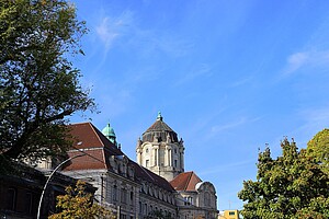 Das majestätische Amtsgericht Charlottenburg mit seiner Kuppel und klassischen Architektur. Der blaue Himmel und Bäume rahmen das Gebäude ein.