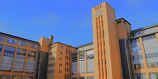 Der Uhrenturm der Osram-Höfe Ein großes Gebäude mit orangefarbenen Backsteinwänden und einem hohen Turm mit einer Uhr an der Spitze. Im Vordergrund ein weitläufiger Platz, umgeben von weiteren Gebäuden.