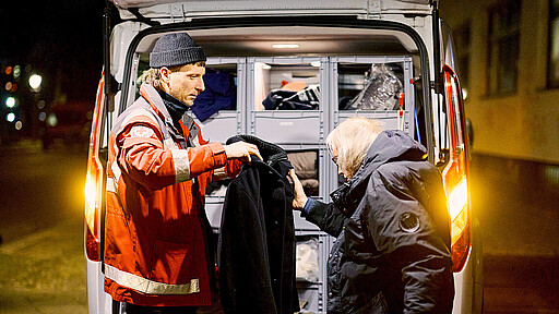 Kältehilfe des DRK für Obdachlose in Berlin: Ein ehrenamtlicher Helfer gibt warme Kleidung an Obdachlose aus.