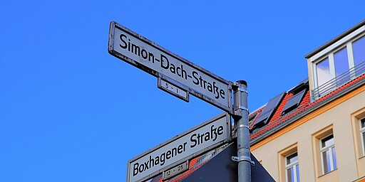 Straßenschild Simon-Dach-Straße und Boxhagener Straße Ein Straßenschild zeigt die Kreuzung von Simon-Dach-Straße und Boxhagener Straße, vor einem tiefblauen Himmel. Das Schild ist an einer Metallstange befestigt und hebt sich vor dem klaren Himmel ab.