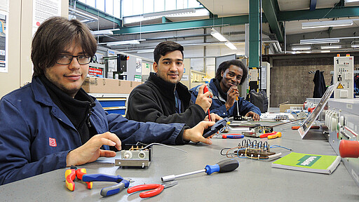 Gruppenfoto Chance+ Chance-Plus-Neueinsteiger Ricardo Loschwitz, Abrar Ali und Ahmed Diallo an der Werkbank.