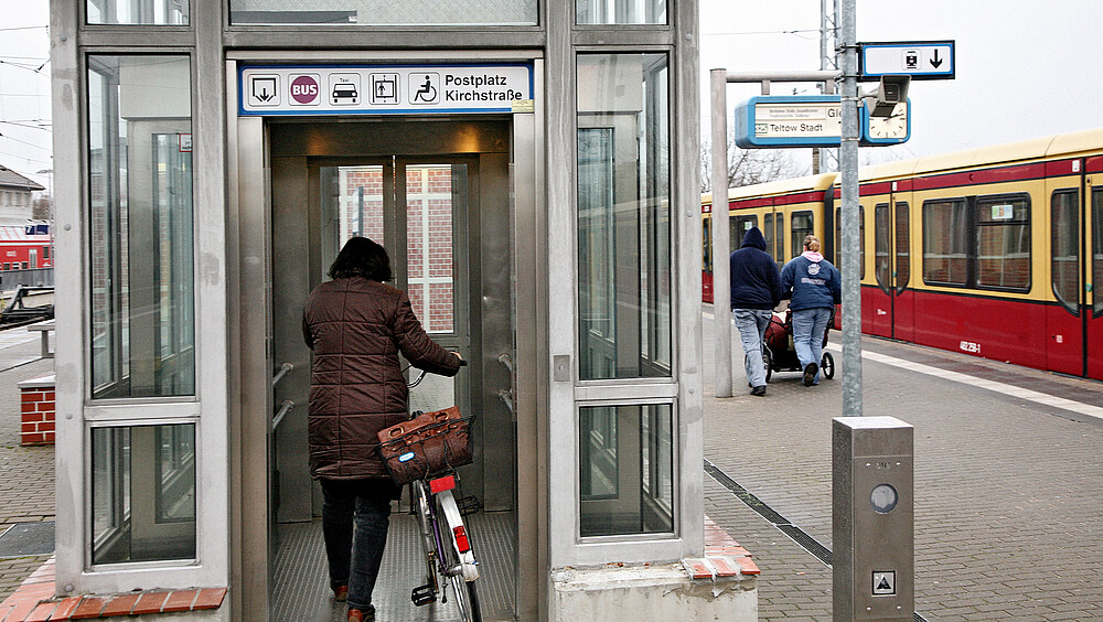 Frau mit Fahrrad geht in den Aufzug am S-Bahnhof Hennigsdorf