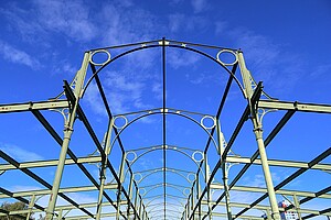 Nahaufnahme der Stahlbögen und Querstreben der Hammelauktionshalle. Der Fokus liegt auf der detailreichen Konstruktion, die sich gegen den strahlend blauen Himmel abhebt.