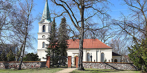 
    
        Die Dorfkirche umringt von alten Mauern und Bäumen
    
