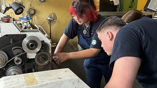 Ausbildung Industriemechaniker:in Sarina Menzlin zeigt Felix Hinz, Azubi im ersten Lehrjahr, wie man die Drehzahl bei der kleinen Drehmaschine richtig einstellt.