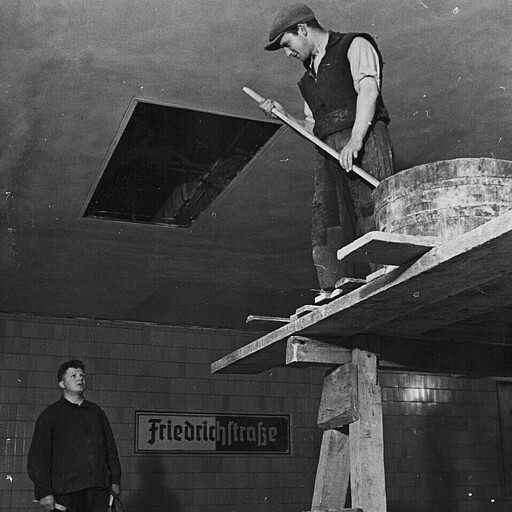 Letzte Arbeiten vor der Eröffnung Wenige Monate vor der Eröffnung beim Ausbau der Tunnelstation: Das Loch in der Decke soll bald den Fahrzielanzeiger aufnehmen. Und beim Bahnhofsnamenschild experimentiert der Architekt Fritz Hane noch: weiß auf schwarz wird es werden.