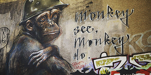 Monkey see, monkey do  Ein Gemälde eines traurigen Affens mit Helm auf einer Mauer