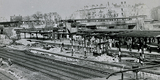 Ostkreuz Der von Luftangriffen schwer gezeichnete Bahnhof Ostkreuz im Sommer 1945 von den Ringbahngleisen gesehen. Am Bahnsteig E im Vordergrund sind die S-Bahngleise der Strecke Berlin–Erkner von der sowjetischen Armee demontiert worden. Der südliche Teil der Fußgängerbrücke ist völlig zerstört, das Empfangsgebäude des Bahnhofs zwischen der Brücke und den Bahnsteigen A und D ist abgebrannt.