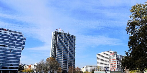 Ernst-Reuter-Platz mit Technischer Universität  Ein Blick auf den Ernst-Reuter-Platz in Berlin. Im Vordergrund sind Grünflächen und ein Wasserbecken zu sehen. Dahinter erhebt sich das markante Hochhaus der Technischen Universität mit dem Schriftzug an der Fassade. Links das schräg stehende Gebäude mit dem Schriftzug "ALSTOM" und rechts das Gebäude mit dem Logo der Deutschen Bank. Der Himmel ist klar und blau, und es herrscht ein sonniger Herbsttag.