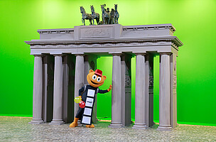 Maskottchen Flimmy steht am Set vom Brandenburger Tor