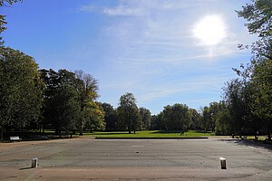 Eine weitläufige Grünfläche im Schillerpark in Berlin, gesäumt von Bäumen mit herbstlich gefärbtem Laub. Im Hintergrund spielen Kinder, während Spaziergänger die friedliche Atmosphäre genießen.