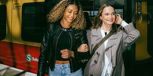 Zwei Frauen eingehakt vor einer S-Bahn der Langlebigkeit Baureihe 481 am Bahnsteig