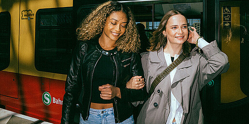 Zwei Frauen eingehakt vor einer S-Bahn der Langlebigkeit Baureihe 481 am Bahnsteig